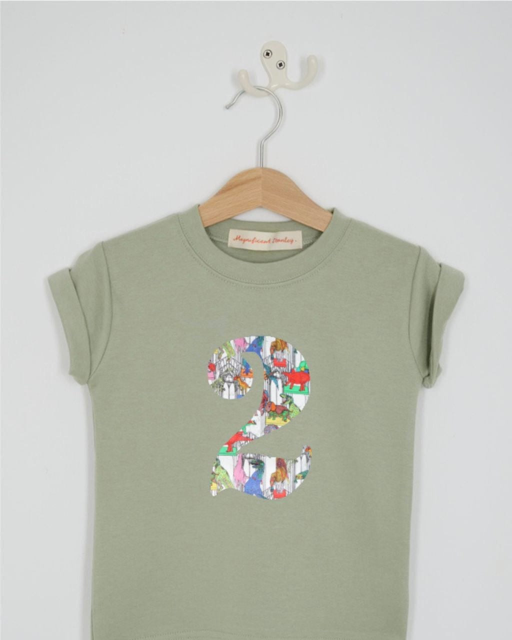 a number 2nd birthday kids sage green t-shirt with a number cut from claws roars n' dinosaurs liberty print on the front.