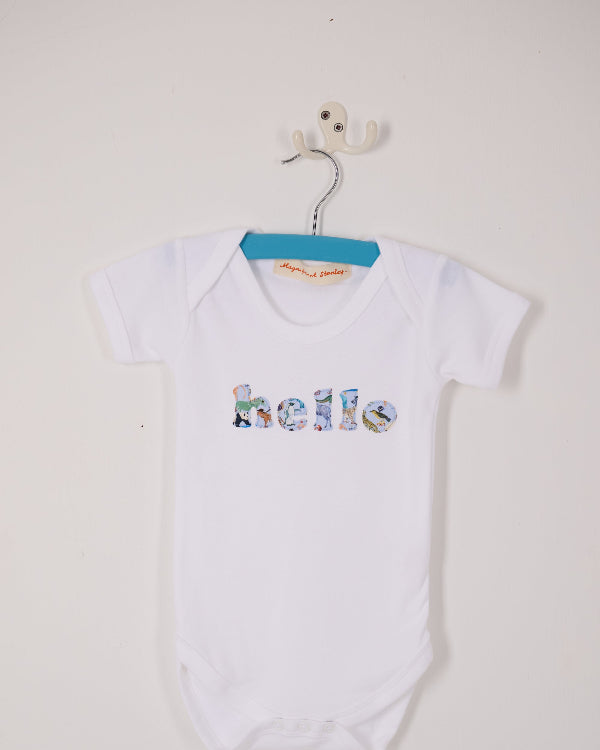 A close up of a white cotton babygrow with the word hello sewn on the front, cut from Quey 2 zoo animal Liberty print.