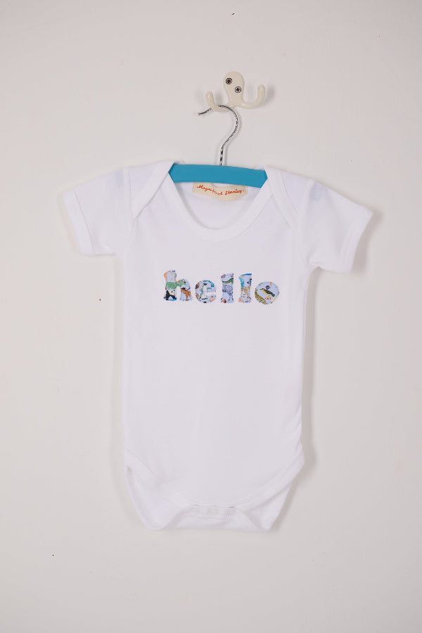 A close up of a white cotton babygrow with the word hello sewn on the front, cut from Quey 2 zoo animal Liberty print.