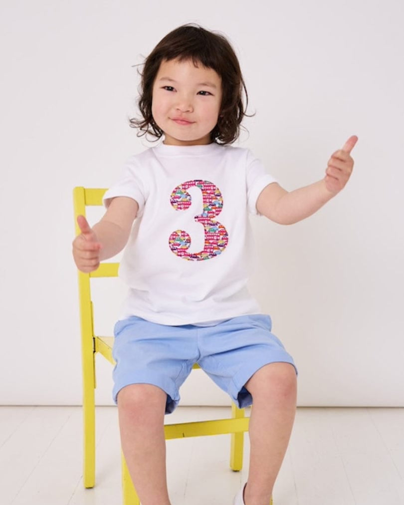 a 3 year old boy is wearing a personalised kids white t-shirt with a number 3 cut from Hop on hop off red cars and london bus liberty print on the front
