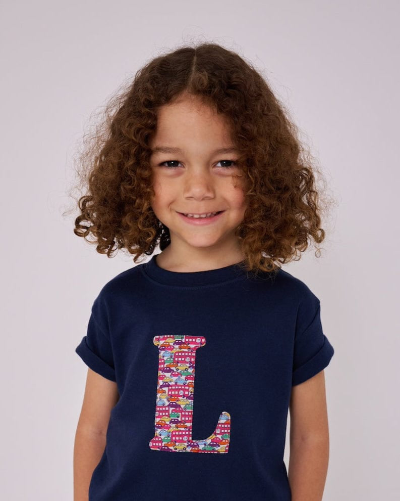 A child wearing a navy t-shirt with the letter 'L' personalised in a red Hop on hop off Liberty print.