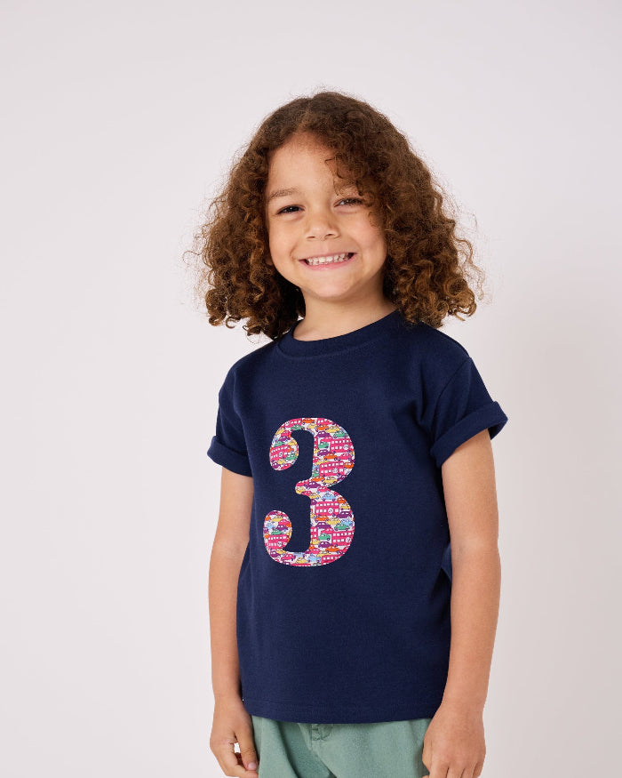 a 3 year old boy wearing a navy cotton kids birthday t-shirt with the number 3 in a red Hop on hop off Liberty print.