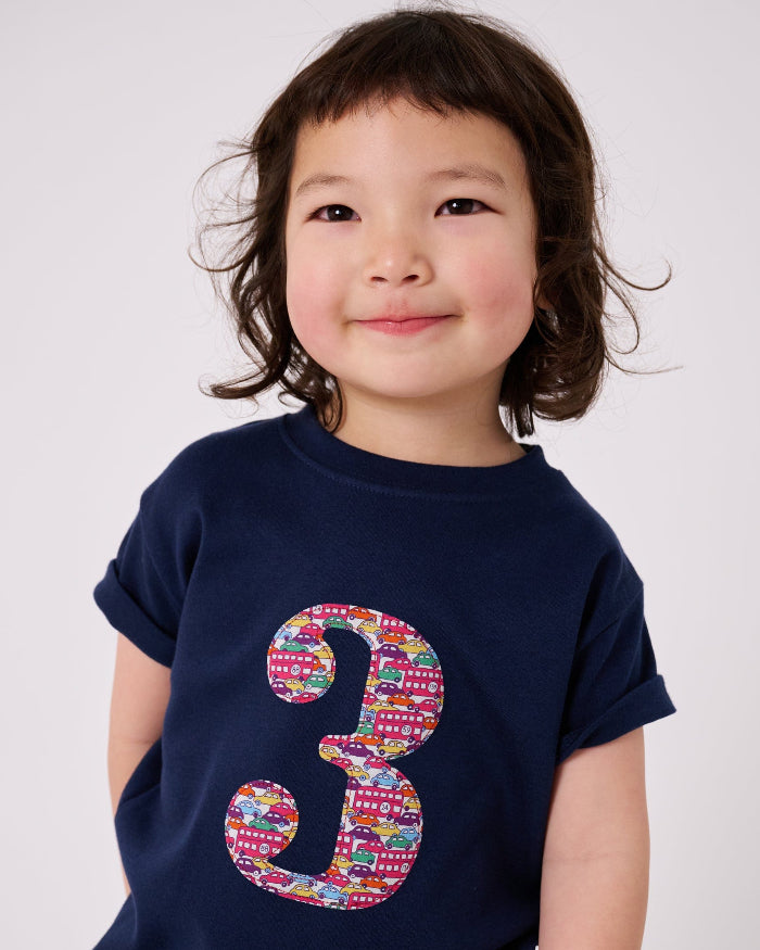 a 3 year old boy wearing a navy cotton kids birthday t-shirt with the number 3 in a red Hop on hop off Liberty print.