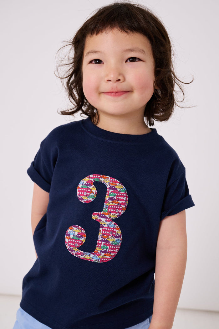 a 3 year old boy wearing a navy cotton kids birthday t-shirt with the number 3 in a red Hop on hop off Liberty print.