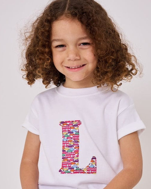 a 4 year old boy is wearing a personalised kids white t-shirt with an initial cut from Hop on hop off red cars and london bus liberty print on the front