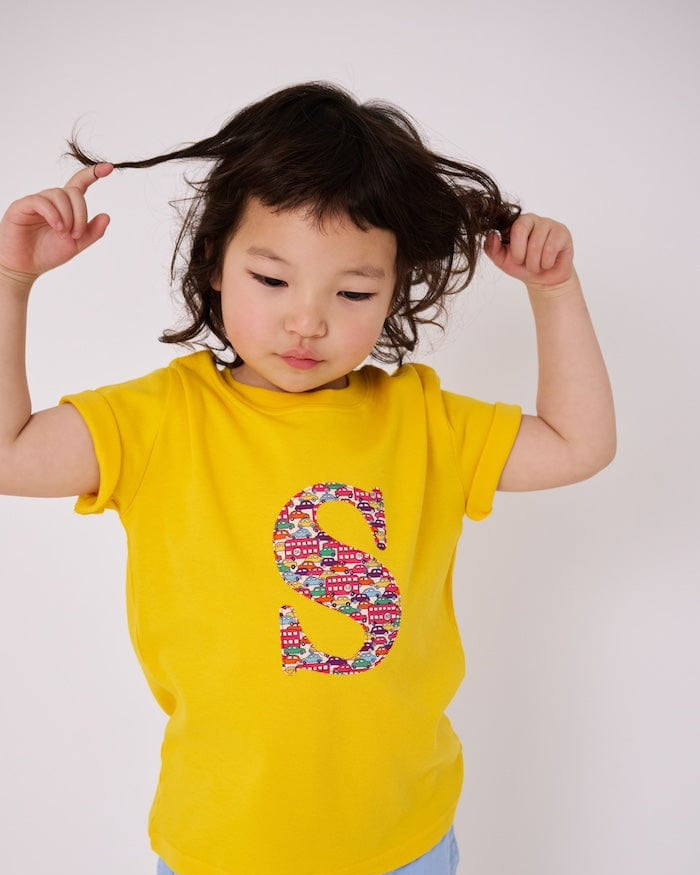 a 4 year old boy is wearing a personalised kids yellow t-shirt with an initial cut from Hop On Hop Off Red Liberty Print on the front