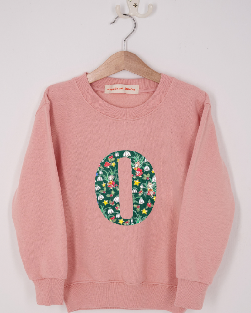 A pink personalised sweatshirt with an initial sewn on to the front. The initial is made from liberty elves print
