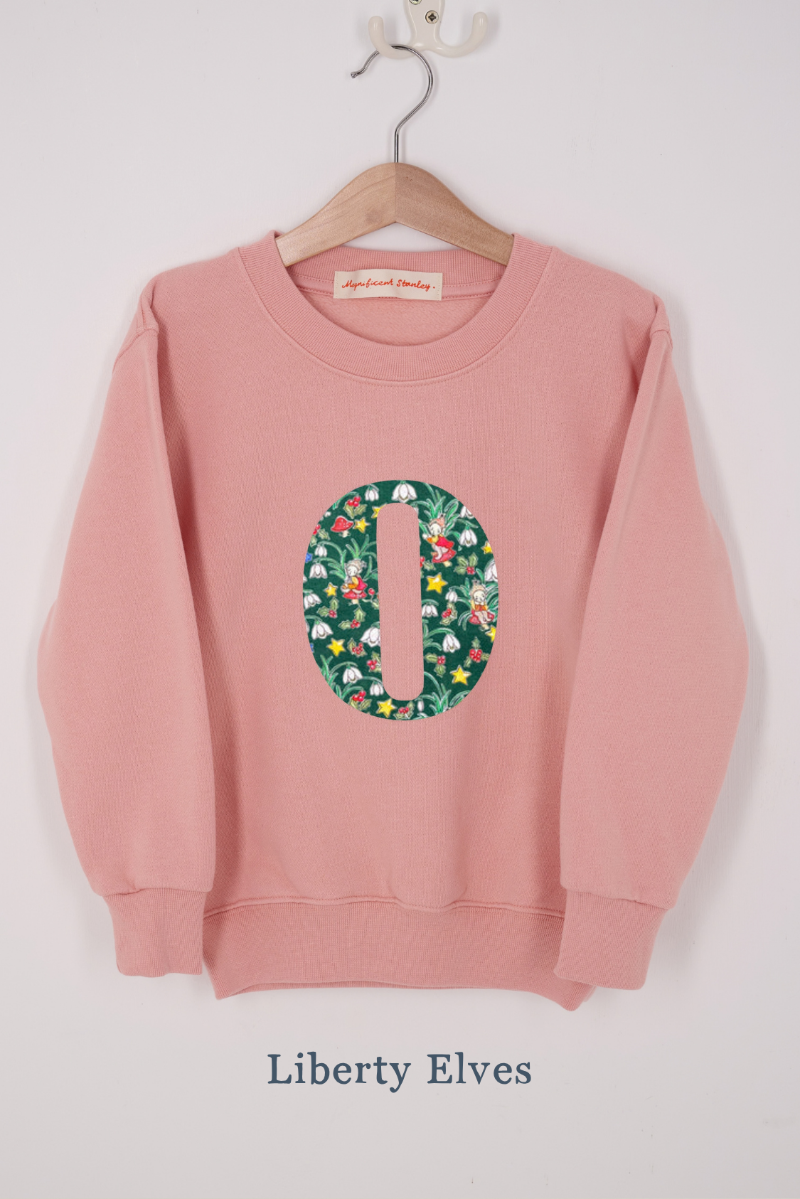 A pink personalised sweatshirt with an initial sewn on to the front. The initial is made from liberty elves print