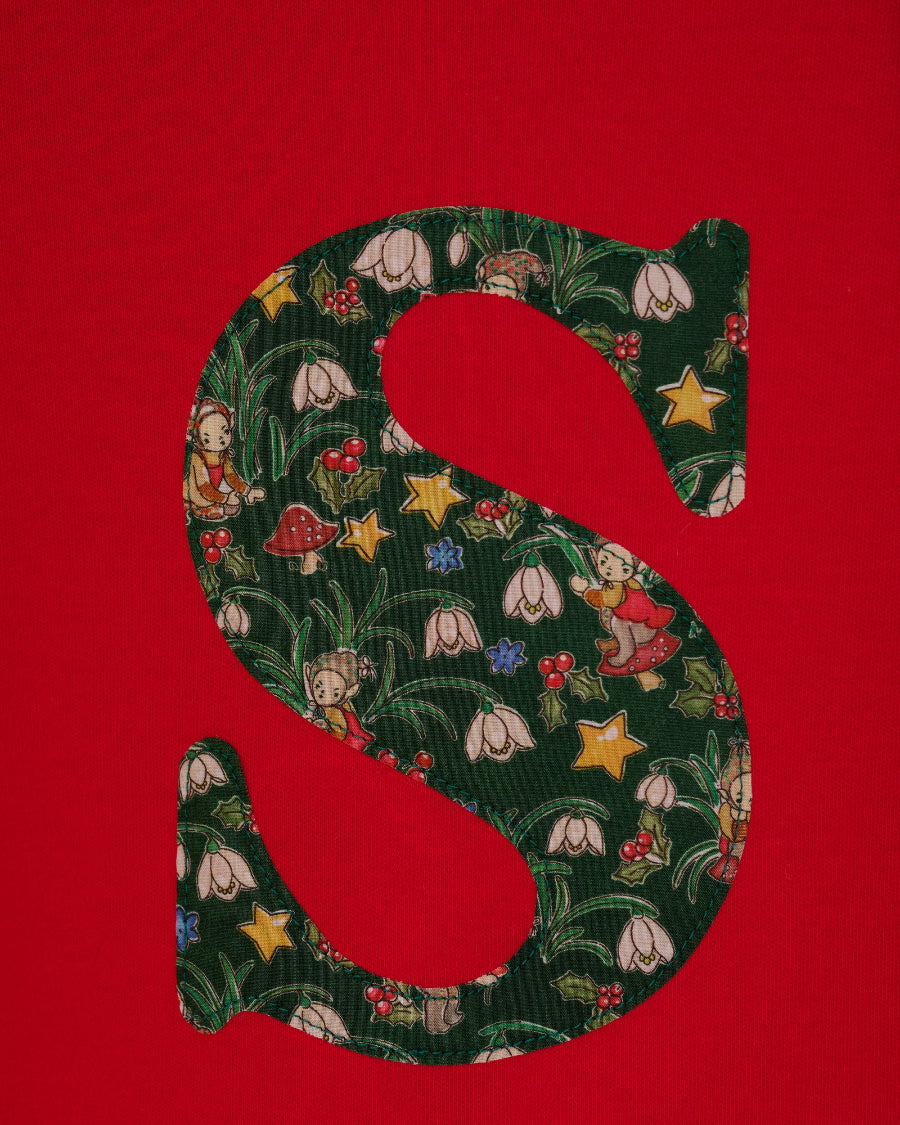 A festive children's outfit set featuring a bright red long-sleeve top with a large green floral monogram letter 'S' on the chest made from Liberty Elves print.