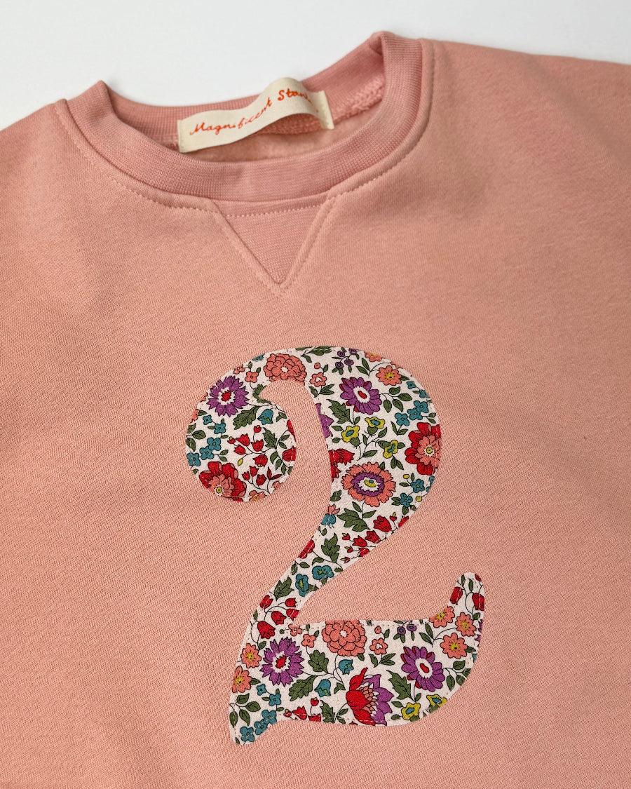 Pink sweatshirt with a liberty floral number '2' on a white background