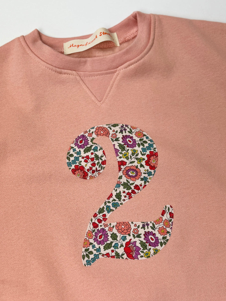Pink sweatshirt with a liberty floral number '2' on a white background