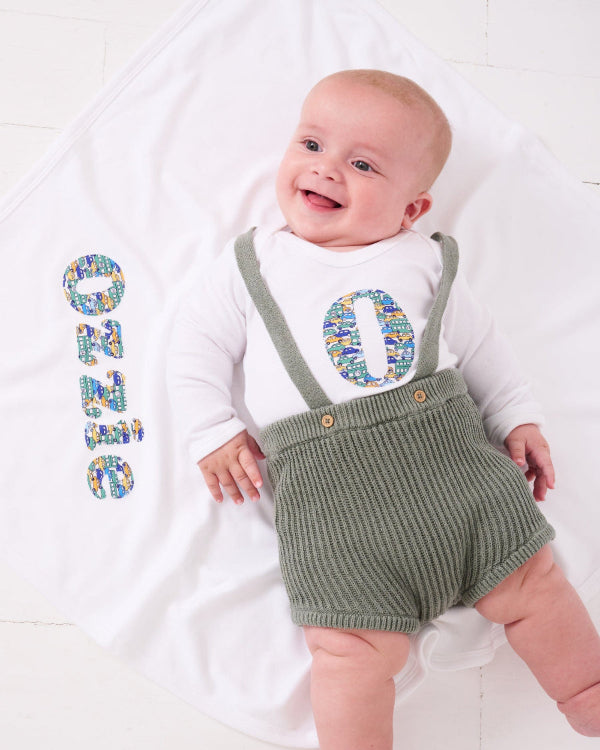 A new baby boy laying on a cotton baby Blanket personalised with his name in cars Liberty print.