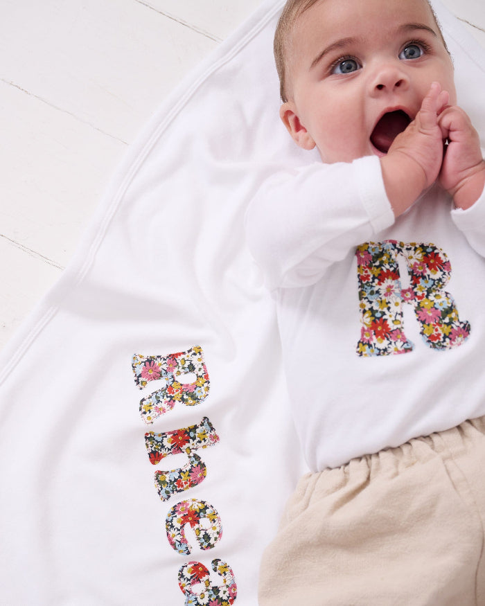 A new baby girl laying on a cotton baby Blanket personalised with her name in Liberty print