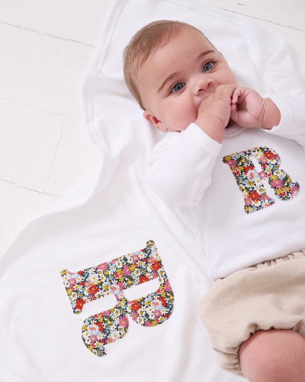 A newborn baby laying on Personalised Liberty Print Cotton Baby Blanket with their initial sewn on it.
