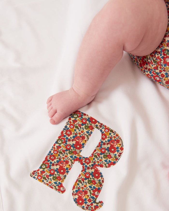 A newborn baby laying on Personalised Liberty Print Cotton Baby Blanket with their initial sewn on it.