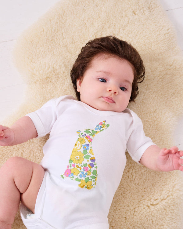 A newborn baby girl wearing a white cotton baby bodysuit with an easter bunny made from Betsy Liberty Print sewn onto the front.