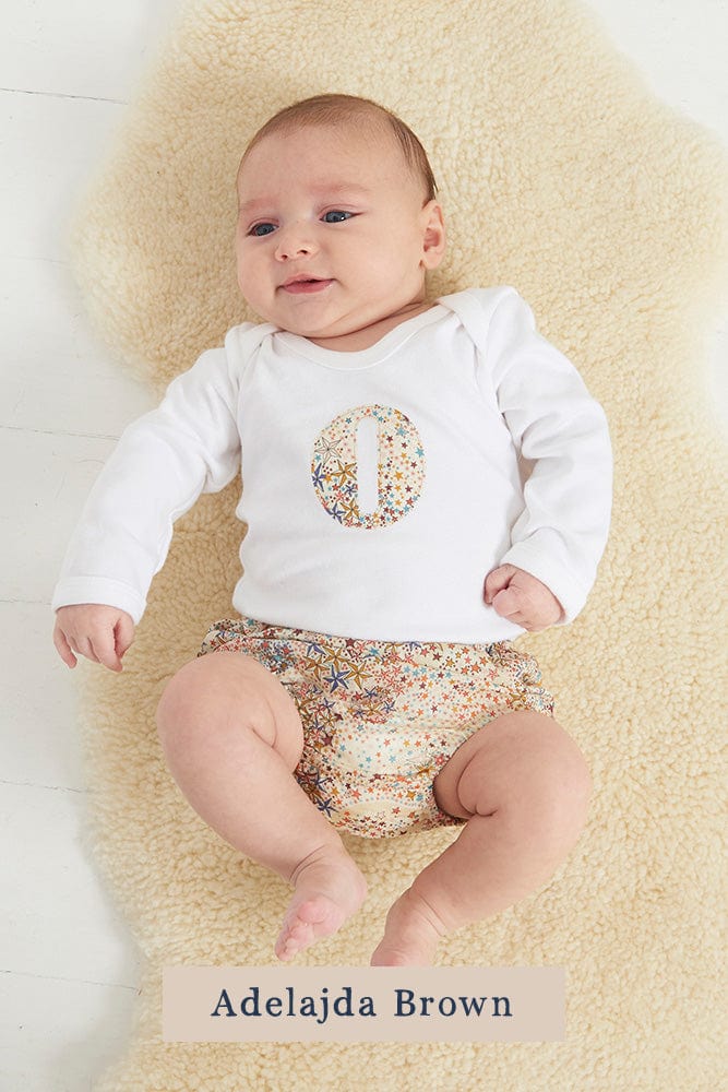 A smiling newborn baby wearing a personalised white bodysuit with an initial on the front cut from Liberty Adelajda starry fabric.