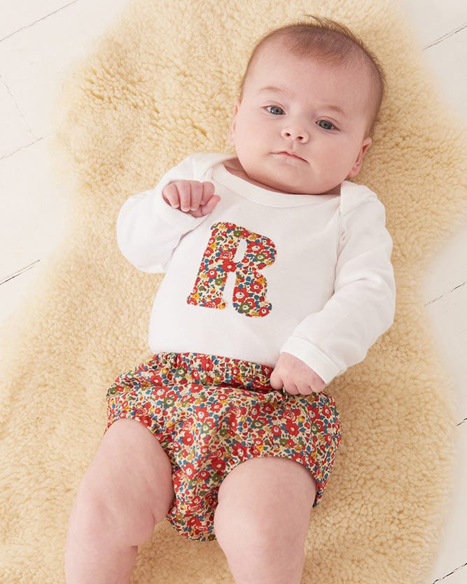 A smiling newborn baby wearing a personalised white bodysuit with an initial on the front cut from Liberty floral fabric.