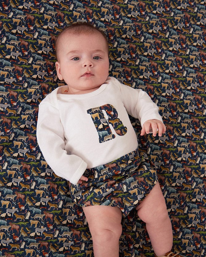 A newborn baby wearing a personalised white bodysuit with an initial on the front cut from Liberty zoo animal fabric.