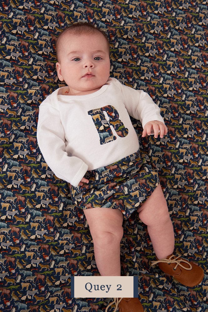 A newborn baby wearing a personalised white bodysuit with an initial on the front cut from Liberty zoo animal fabric.