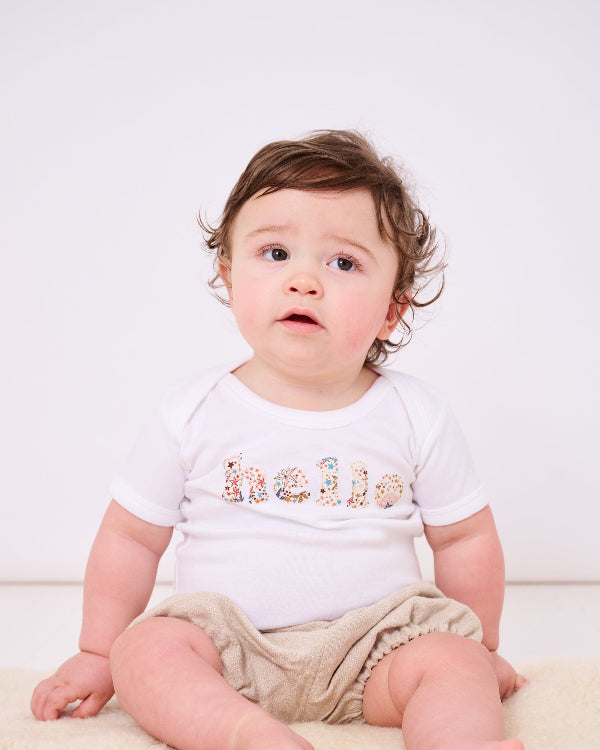 Magnificent Stanley Bodysuit 'hello' Bodysuit. New baby wears a white bodysuit with the word hello on it. the letters are cut from starry liberty print