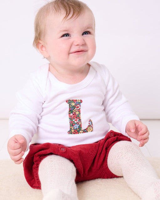 A baby wearing a personalised baby grow with her initial on cut from Liberty Emma Louise cotton fabric.