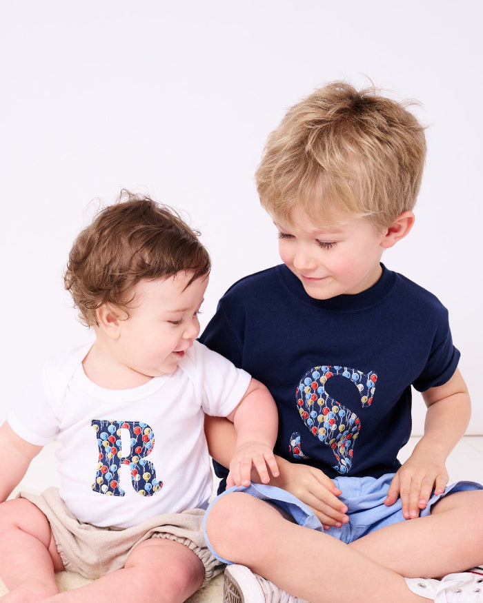 A baby wearing a Personalised Bodysuit in Ethan's Party Liberty Print with his brother wearing a matching personalised kids t-shirt