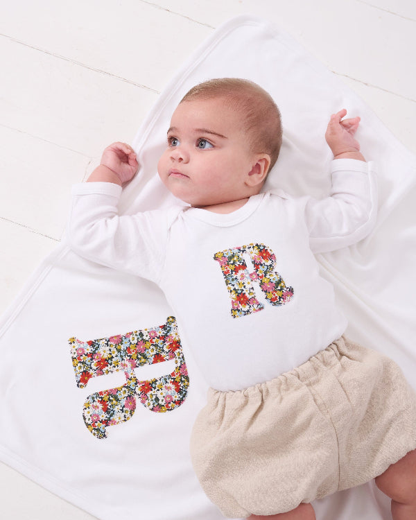 A newborn baby girl wearing a Personalised baby Bodysuit in Libby floral Liberty Print. She is laying on a personalised cotton baby blanket