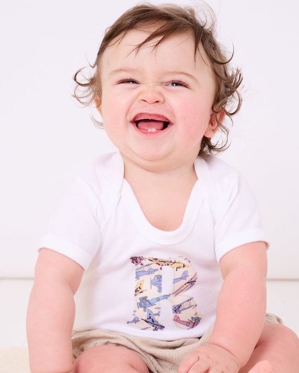 A 6 month old baby boy wearing a Personalised Bodysuit in Tom's Jet Liberty Print with his initial sewn onto the front.
