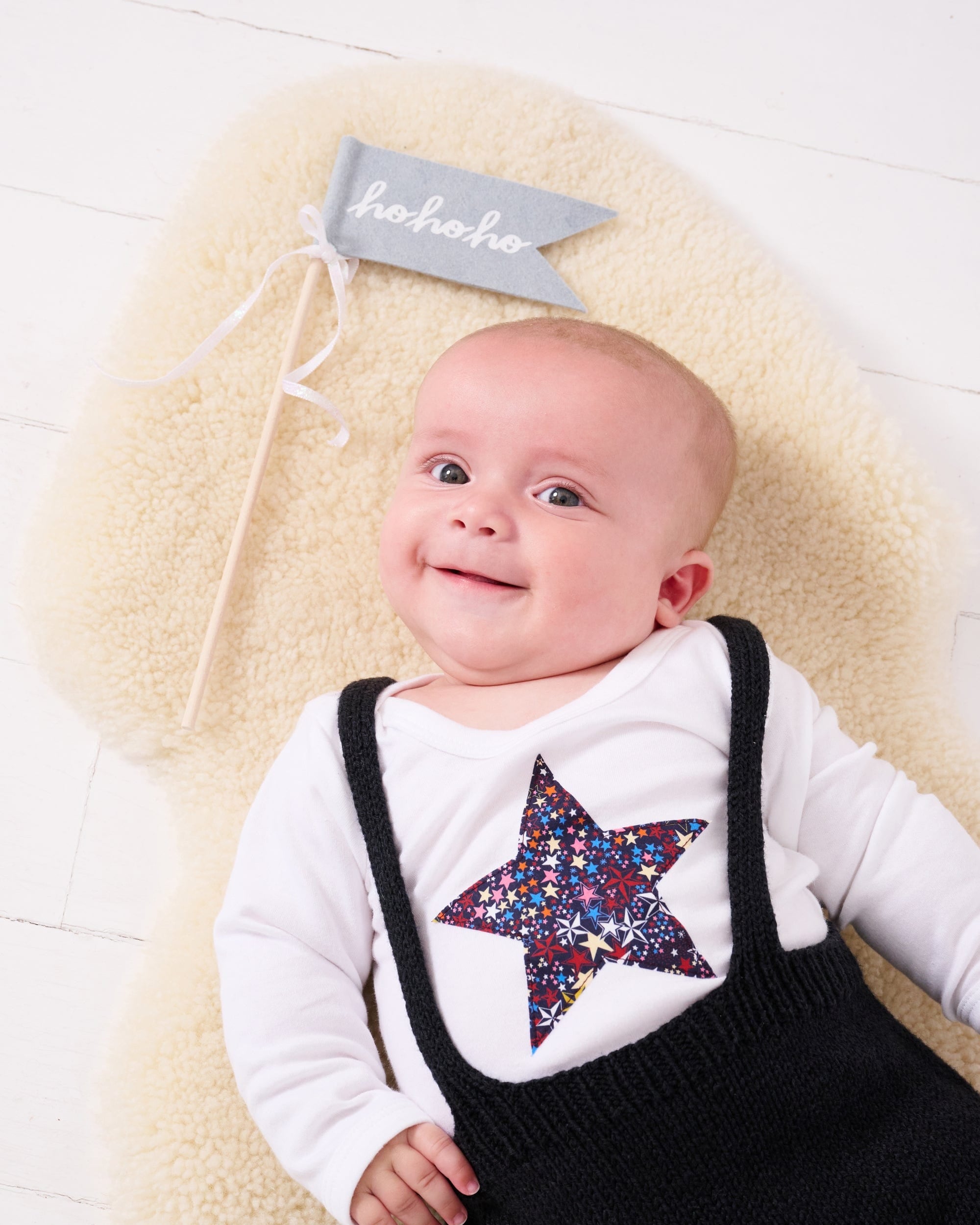 A baby wearing a white bodysuit babygrow with a Liberty Adelajda's Wish print festive star sewn on the front.