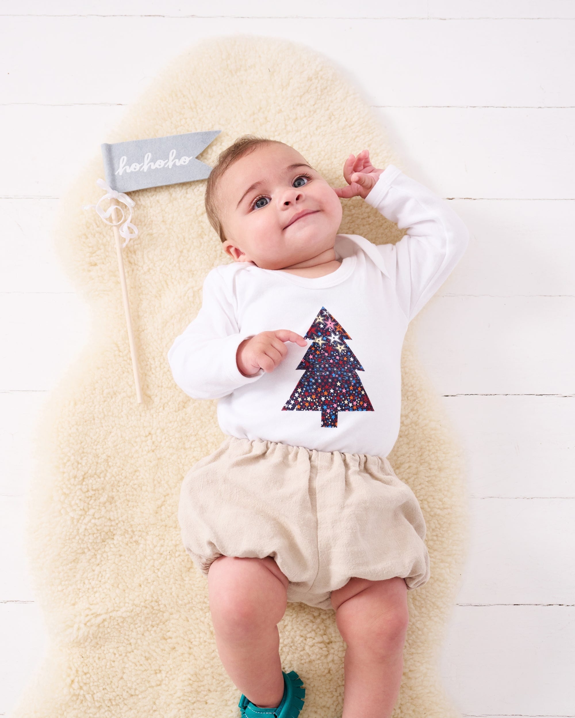 A baby wearing a white bodysuit babygrow with a Liberty Adelajda's Wish print Christmas tree sewn on the front.