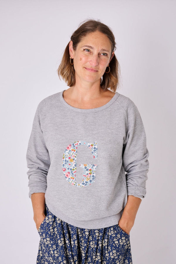 A lady wearing a personalised Ladies Grey Ladies Sweatshirt, with her initial on the front cut from Betsy Liberty print.