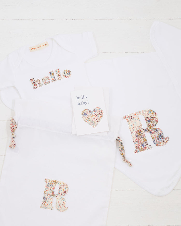 a personalised baby gift set consisting of a hello baby card, a personalised bodysuit, personalised cotton baby blanket and a gift bag, all personalised with Liberty print.