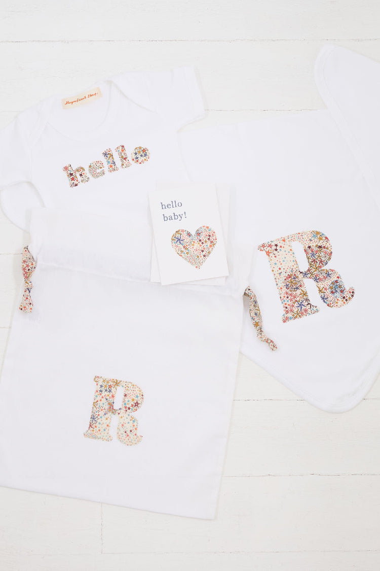 a personalised baby gift set consisting of a hello baby card, a personalised bodysuit, personalised cotton baby blanket and a gift bag, all personalised with Liberty print.