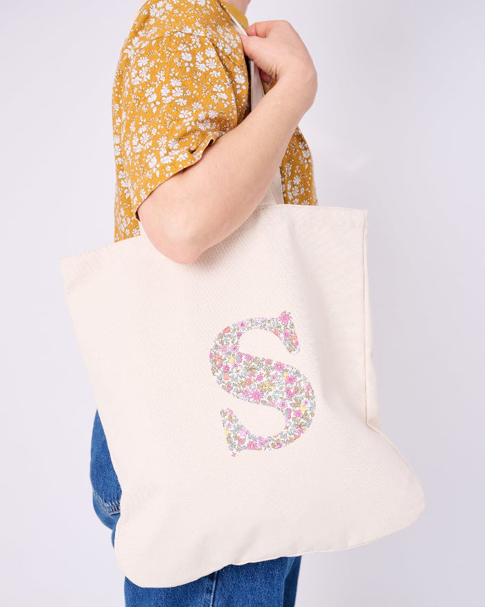 A woman with a Canvas Tote Bag on her shoulder, personalised with her initial in Liberty ditsy floral fabric