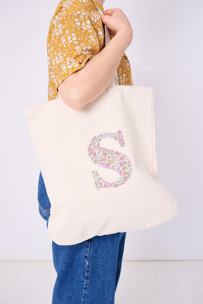 A woman with a Canvas Tote Bag on her shoulder, personalised with her initial in Liberty ditsy floral fabric