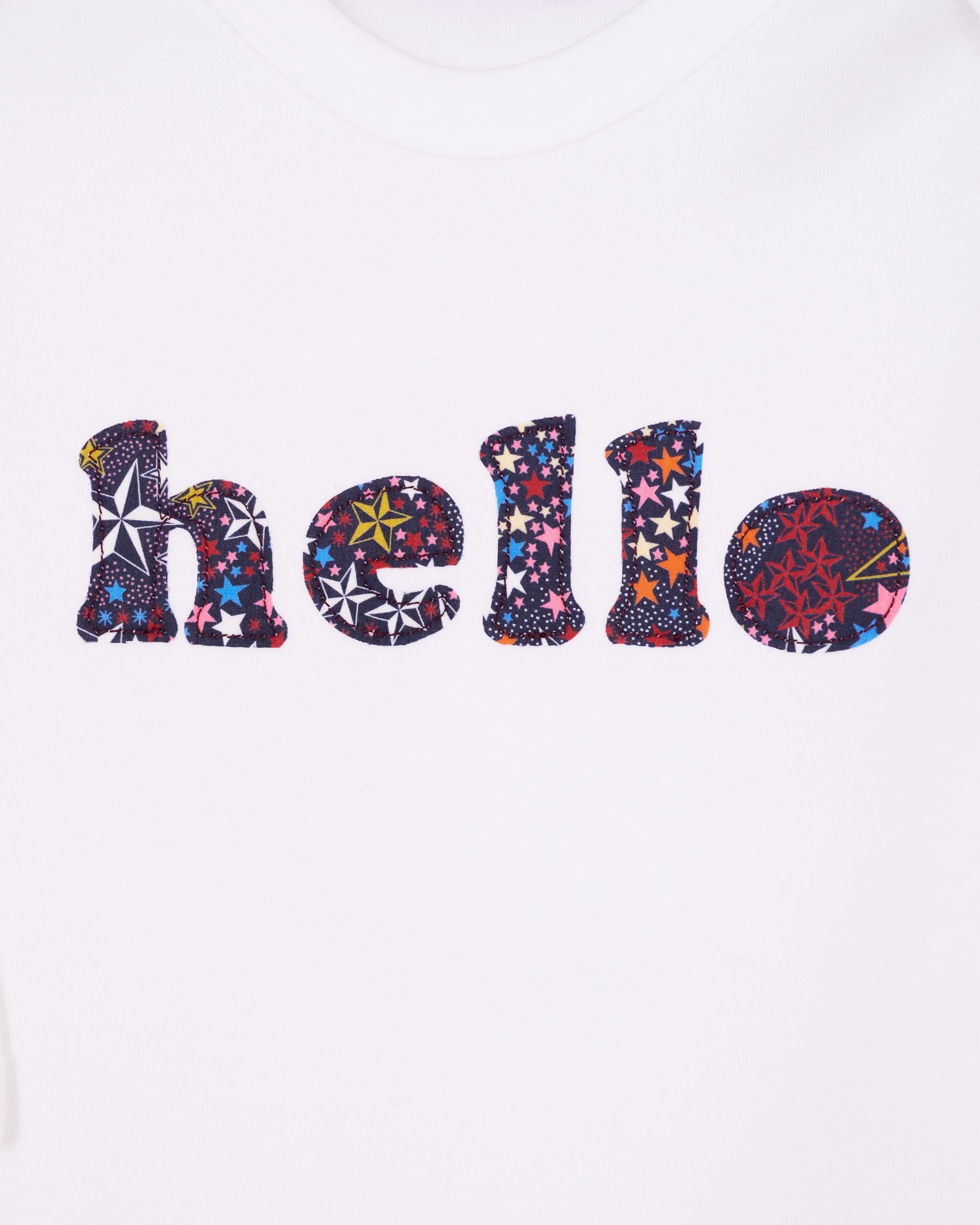 Close up of a white cotton romper with the word hello on it. the letters are cut from starry liberty print and appliquéd onto the romper