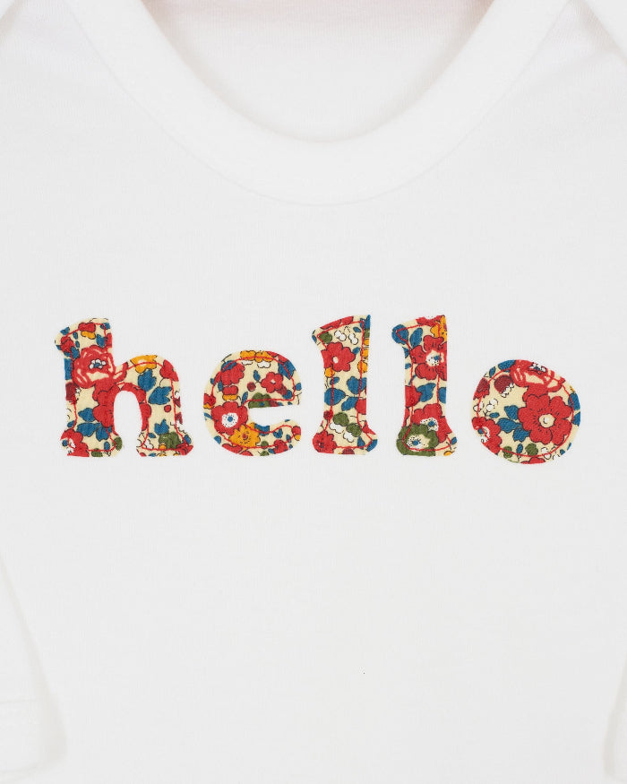 Close up of a white cotton romper with the word hello on it. the letters are cut from floral liberty print and appliquéd onto the romper