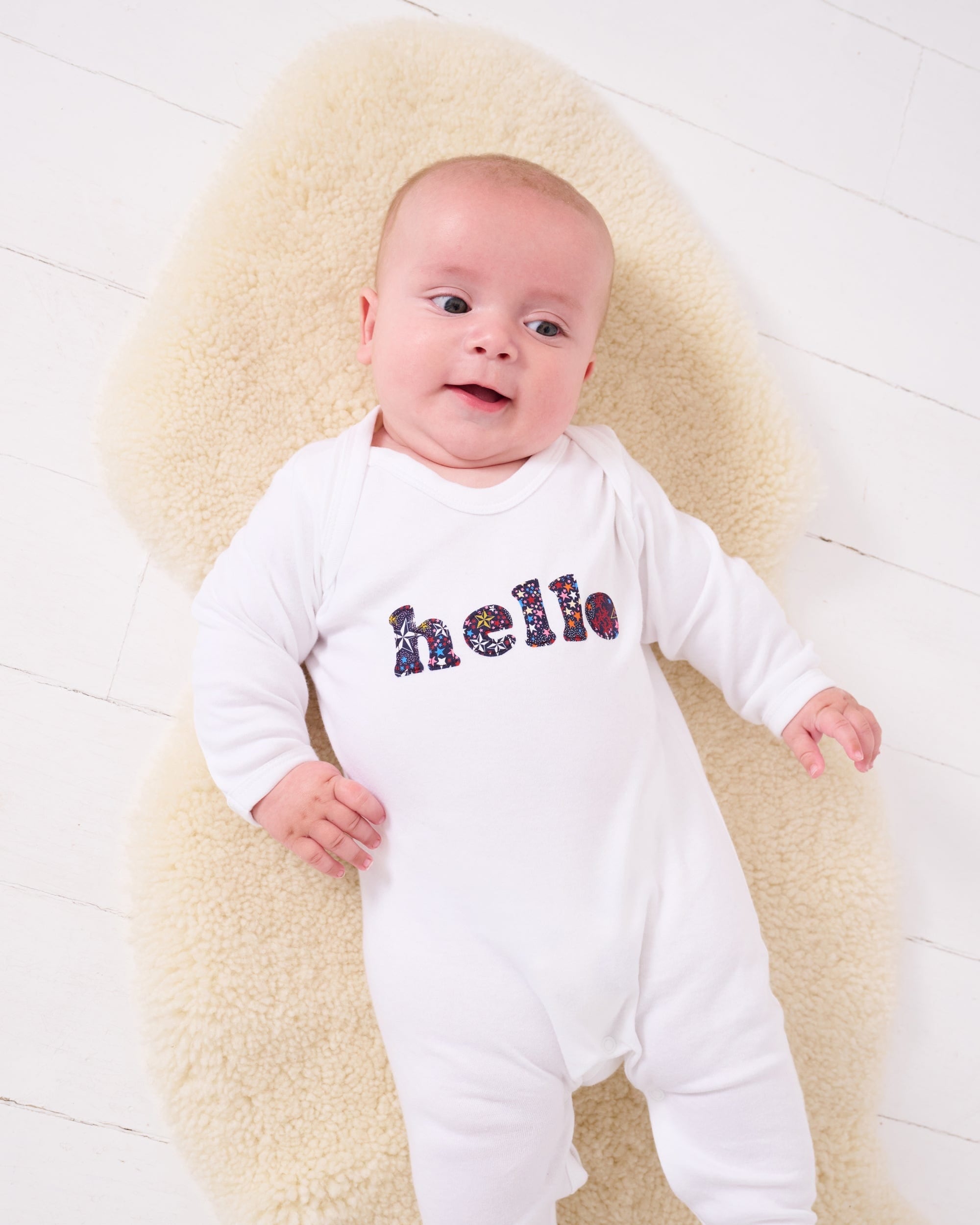A new baby wears a white cotton romper with the word hello on it. the letters are cut from starry liberty print