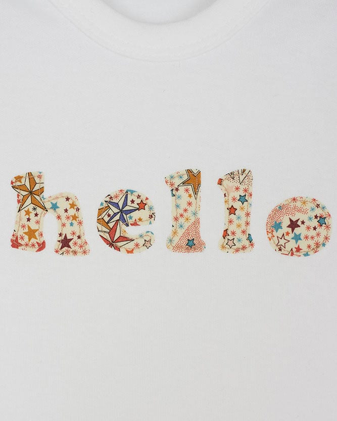 Close up of a white cotton romper with the word hello on it. the letters are cut from adelajda star liberty print and appliquéd onto the romper