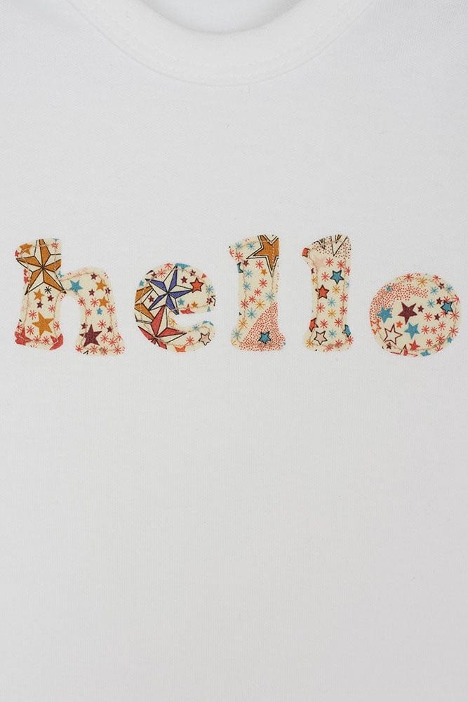 Close up of a white cotton romper with the word hello on it. the letters are cut from adelajda star liberty print and appliquéd onto the romper