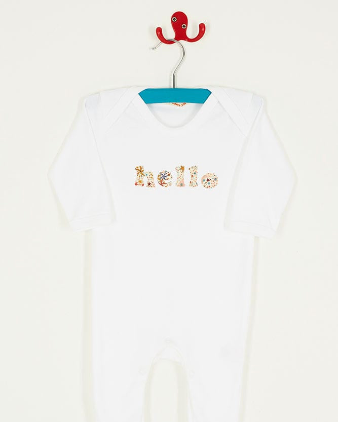 Close up of a white cotton romper with the word hello on it for a new baby. the letters are cut from adelajda star liberty print and appliquéd onto the romper