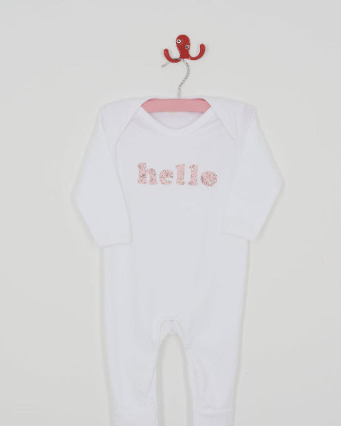Close up of a white cotton romper with the word hello on it. the letters are cut from Capel floral liberty print and appliquéd onto the romper.