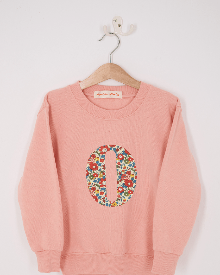 A pink personalised sweatshirt with an initial sewn on to the front. The initial is made from floral Betsy Ann liberty print.