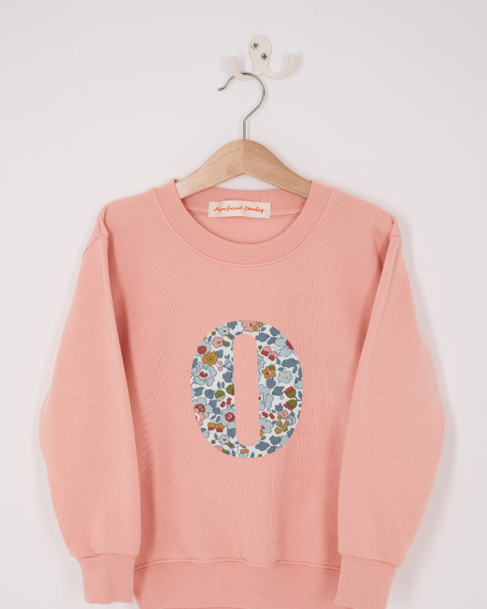 A pink personalised sweatshirt with an initial sewn on to the front. The initial is made from Betsy Grey floral liberty print