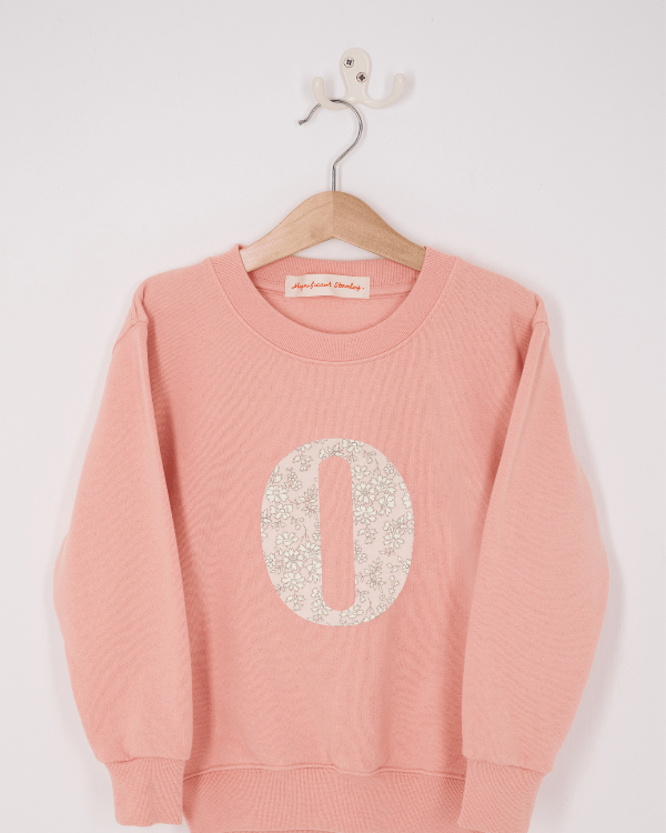 A pink personalised sweatshirt with an initial sewn on to the front. The initial is made from Capel floral liberty print