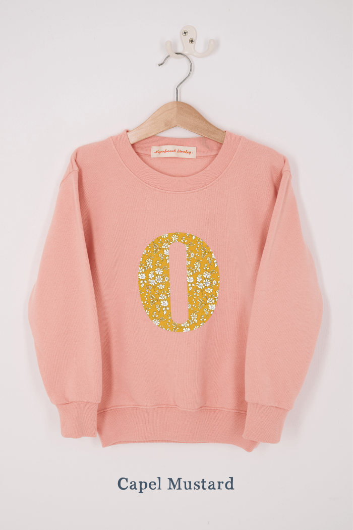 A pink personalised sweatshirt with an initial sewn on to the front. The initial is made from floral Capel liberty print