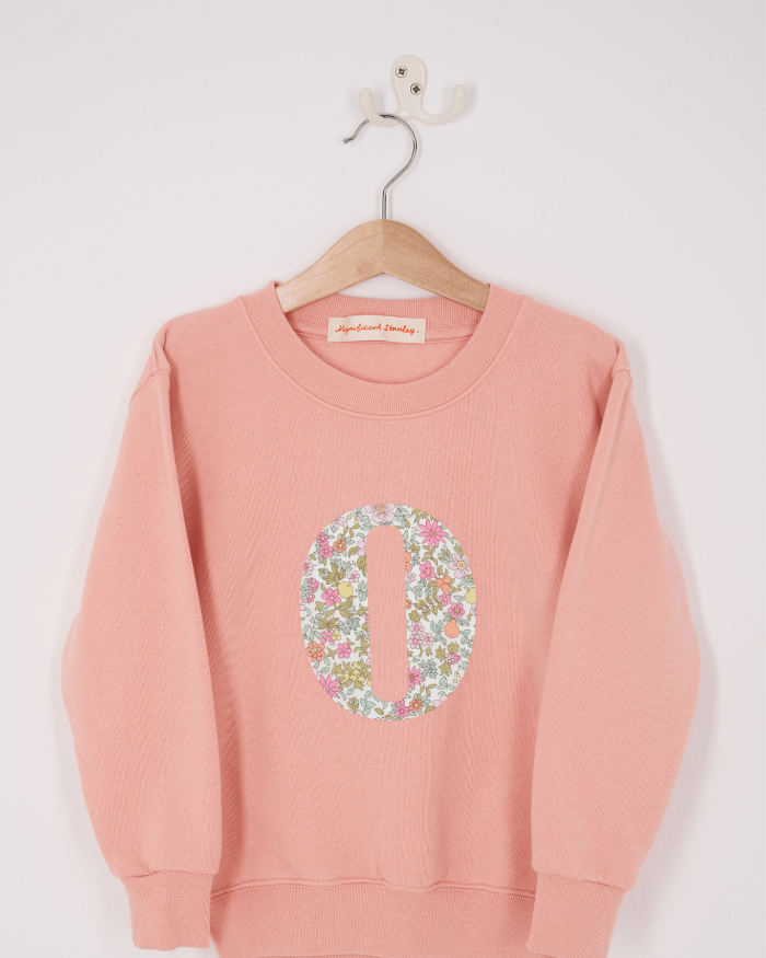 A pink personalised sweatshirt with an initial sewn on to the front. The initial is made from pink floral liberty print