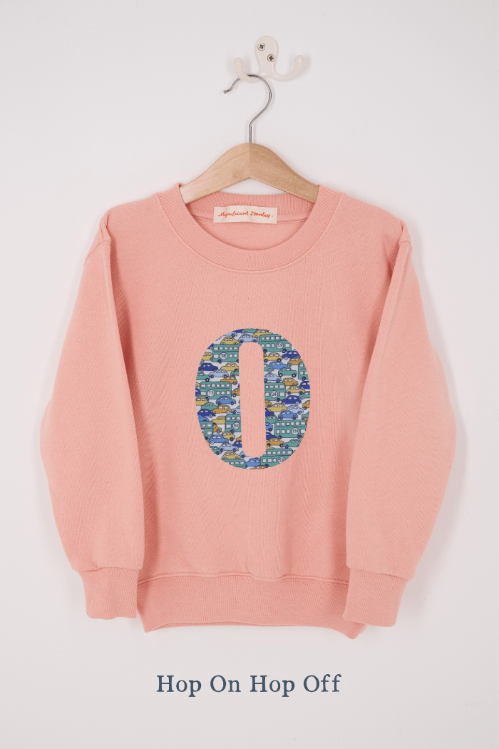 A pink personalised sweatshirt with an initial sewn on to the front. The initial is made from vintage car liberty print