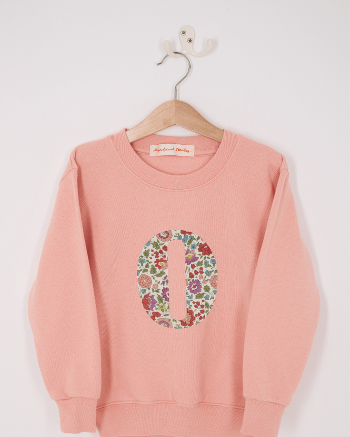A pink personalised sweatshirt with an initial sewn on to the front. The initial is made from D'Anjo floral liberty print